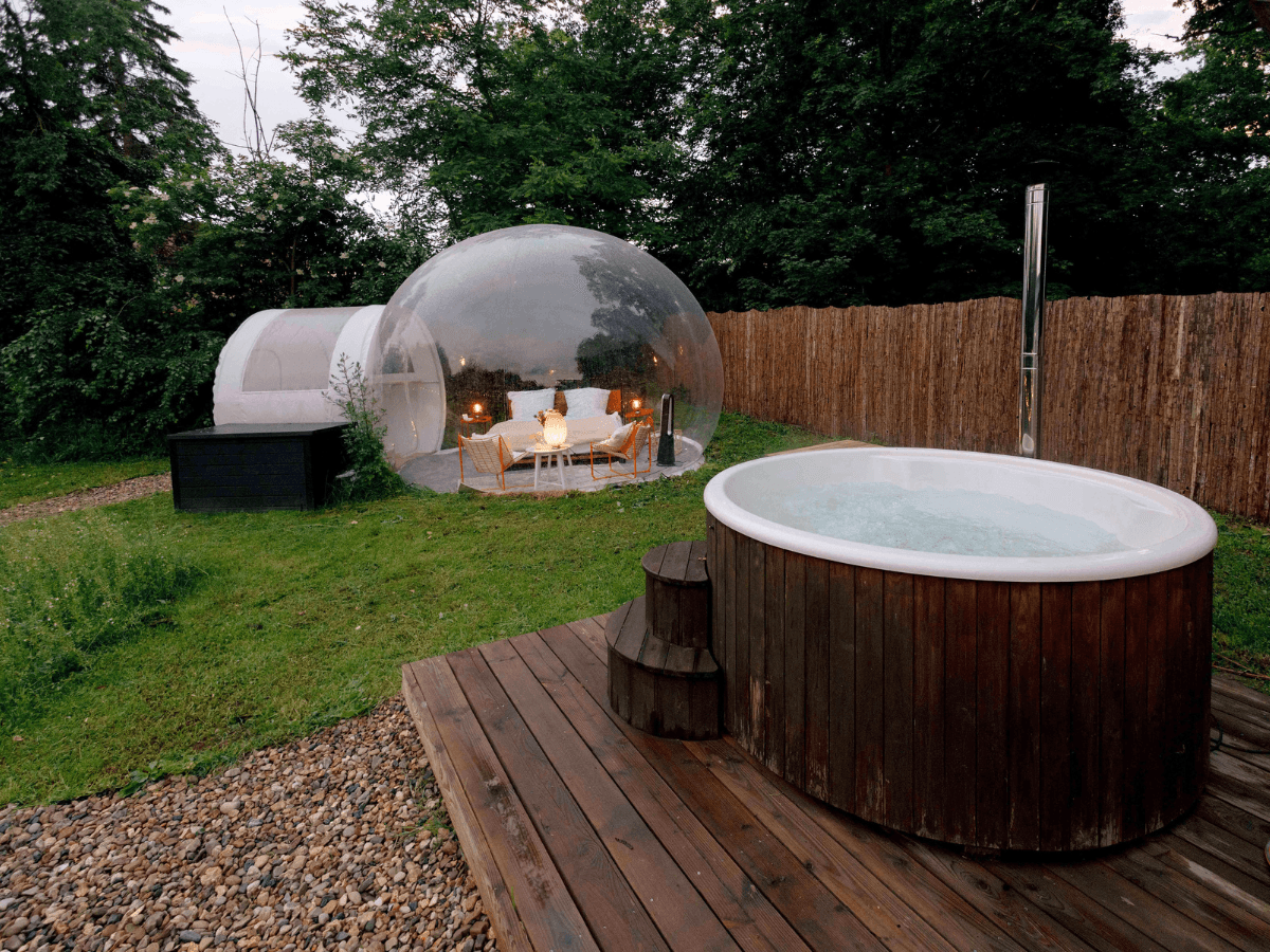 Bubble Zelt mit beleuchtetem Doppelbett und Whirlpool - romantische Bubble Tent Übernachtung in der Abenddämmerung.