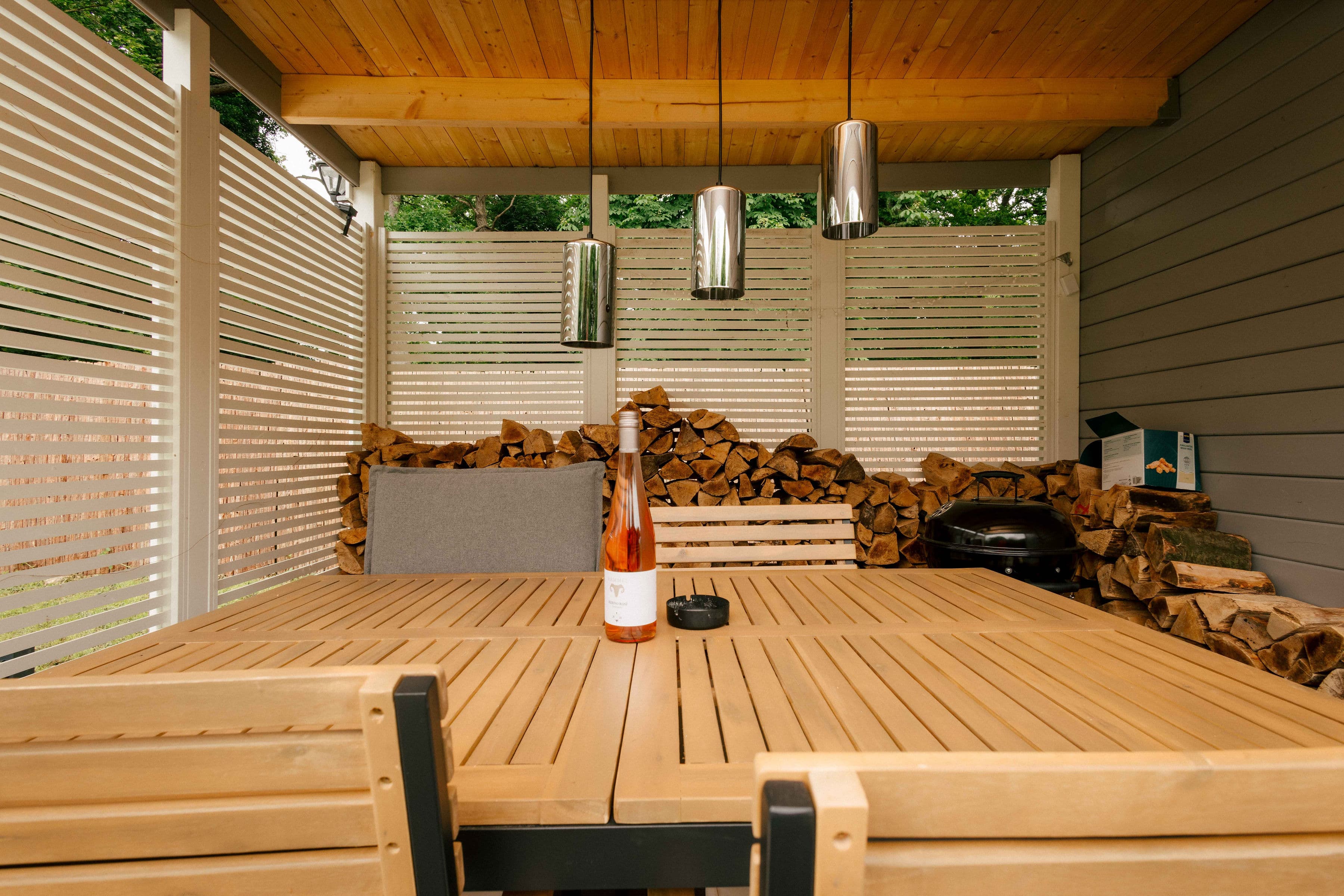 Überdachte Lounge-Veranda mit Holztisch, Feuerholz und Grill am Bubble Zelt – gemütlicher Rückzugsort für laue Abende.
